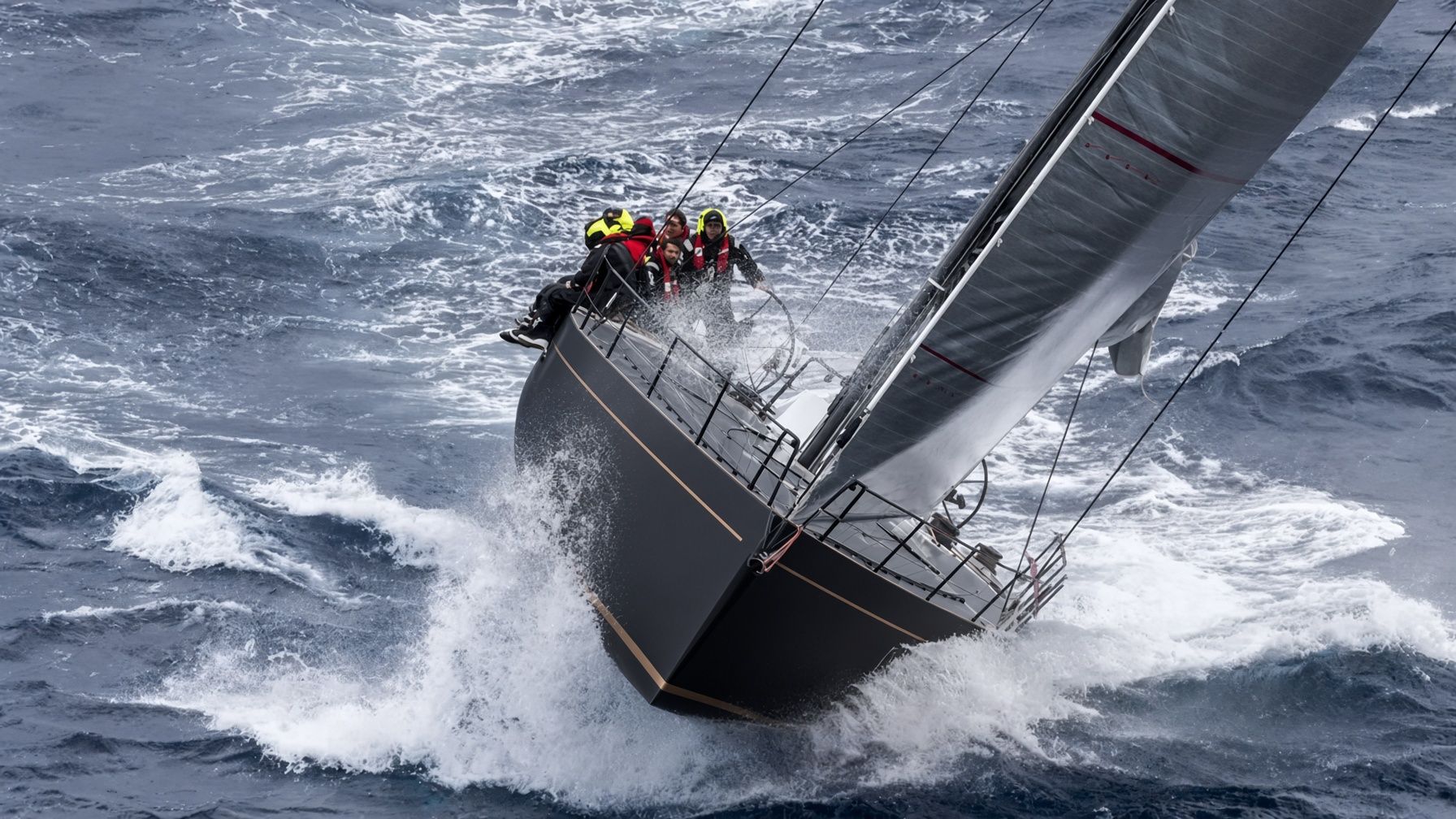 A racing yacht crew holds a steady course through rough, white-capped water